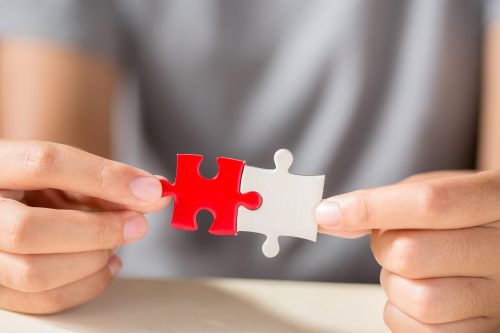 hand connecting two puzzle pieces on table background, business strategy concept